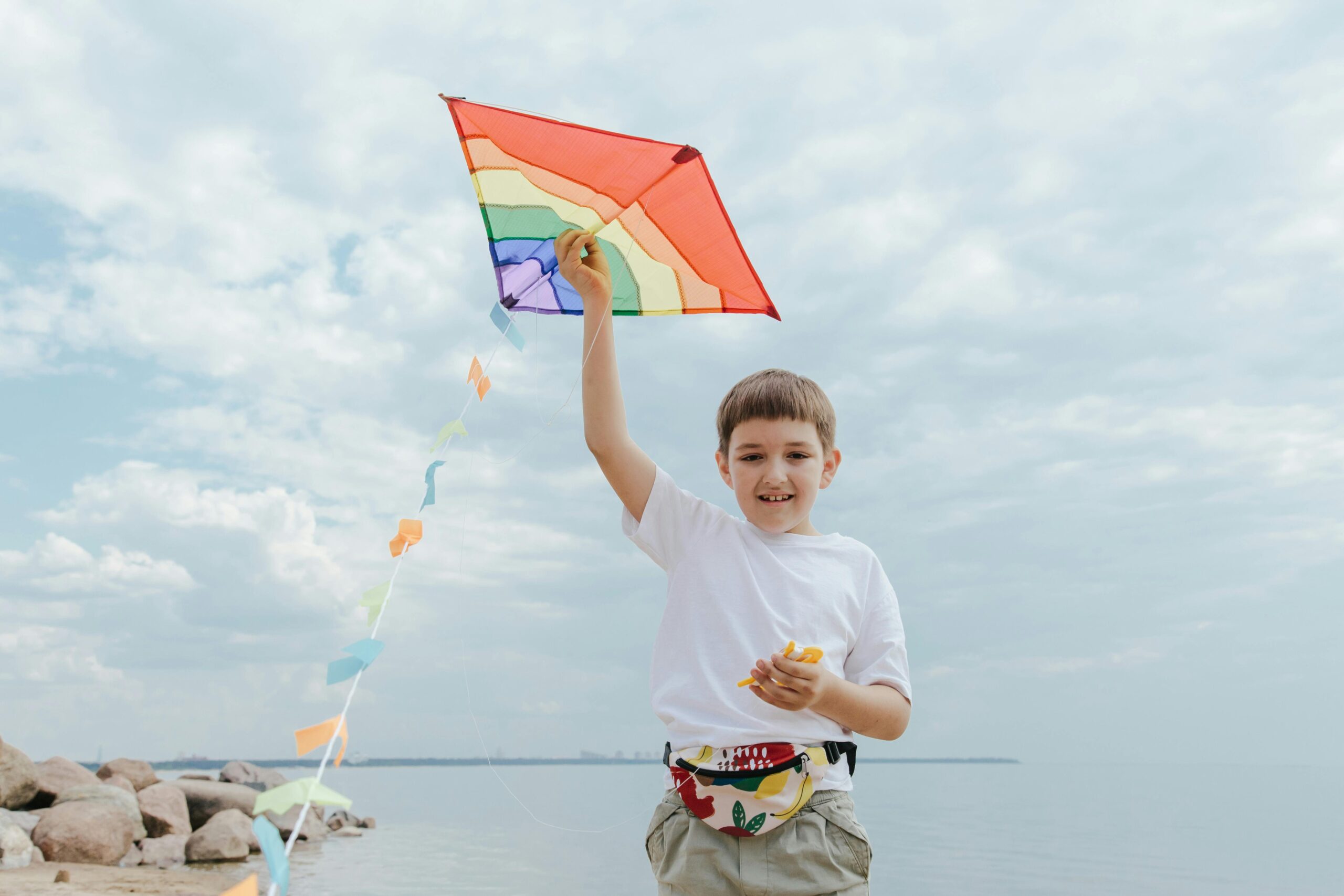 Young boy joyfully flies a colorful kite on a breezy beach day, experiencing simple outdoor fun.